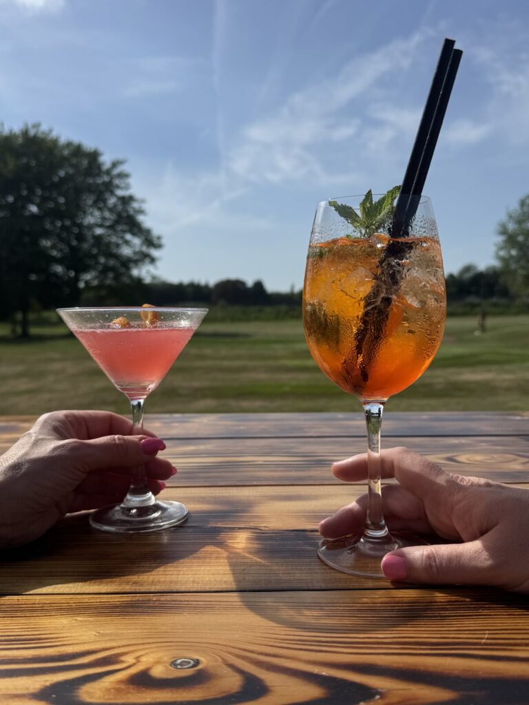 cosmopolitan and aperol spritz on a wooden table overlooking a golf course in a bicester pub garden